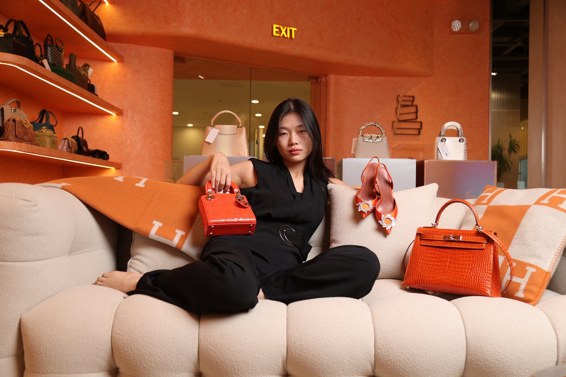 Model surrounded by curated designer bags and accessories inside The Orange Box, a luxury bag shop in BGC, Philippines.